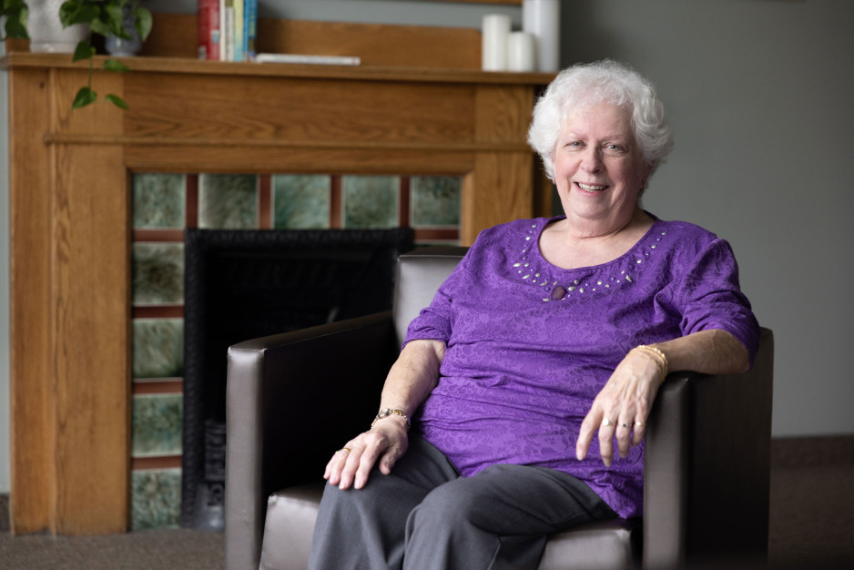 Nancy sits near a fireplace