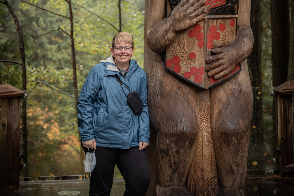 A woman (Ashley Camden) in a forest leaning up against a totem pole