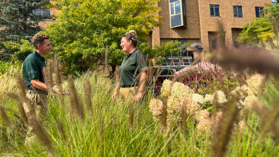 Clintar landscaping workers standing in a field with tall grass and a hospital building in the background