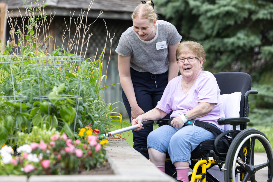 a woman in a wheelchair gardening with the assistance of a tool as her care provider watches