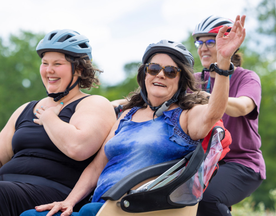 A patient waves from the triobike with care providers in tow